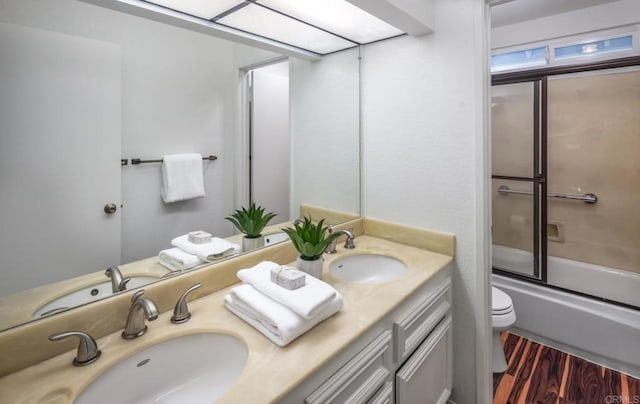 full bathroom with wood-type flooring, bath / shower combo with glass door, toilet, and vanity