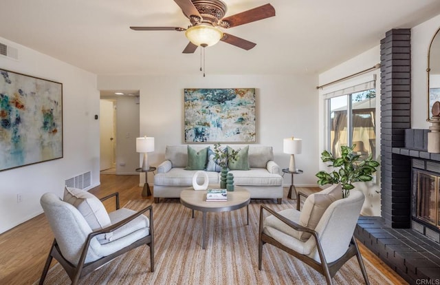 living room featuring a brick fireplace, light hardwood / wood-style flooring, and ceiling fan