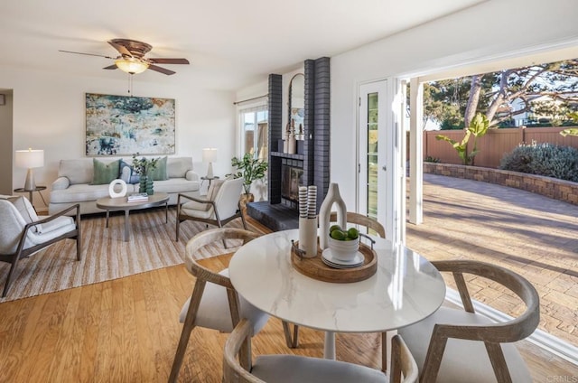 dining area with ceiling fan, a fireplace, and light wood-type flooring