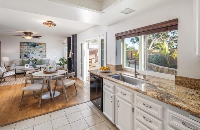 kitchen with light tile patterned floors, ceiling fan, black dishwasher, white cabinets, and sink