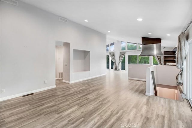 unfurnished living room featuring visible vents, baseboards, and wood finished floors