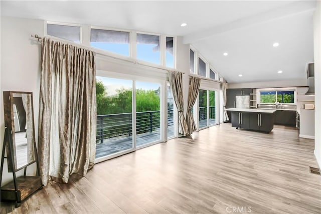 unfurnished living room with high vaulted ceiling, light wood-type flooring, a wealth of natural light, and beamed ceiling