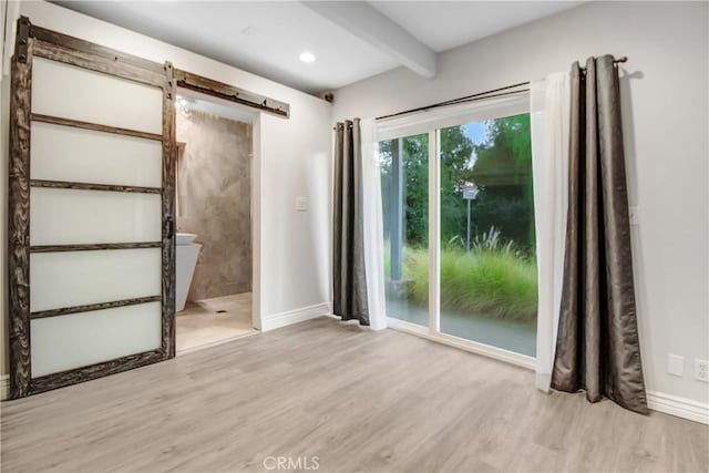 empty room featuring beam ceiling, a barn door, and light hardwood / wood-style flooring