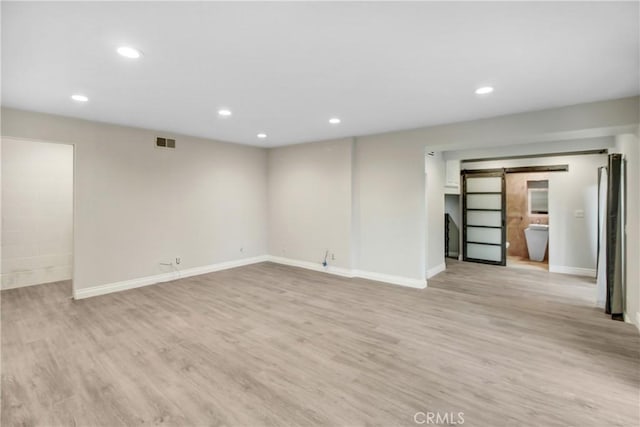 finished basement with visible vents, light wood-type flooring, a barn door, and recessed lighting
