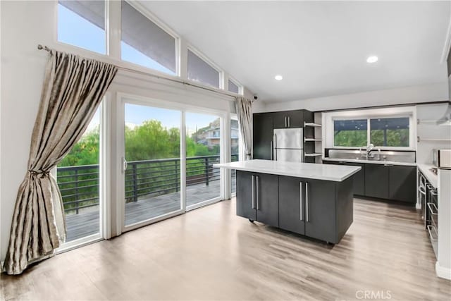 kitchen featuring high vaulted ceiling, light hardwood / wood-style flooring, stainless steel refrigerator, and a center island