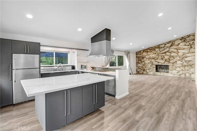 kitchen featuring a kitchen island, a wealth of natural light, light stone countertops, appliances with stainless steel finishes, and island range hood