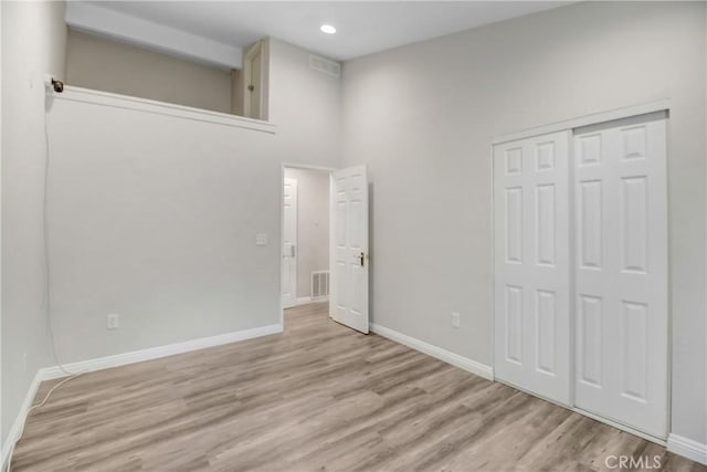 unfurnished bedroom with a closet, a high ceiling, and light hardwood / wood-style floors