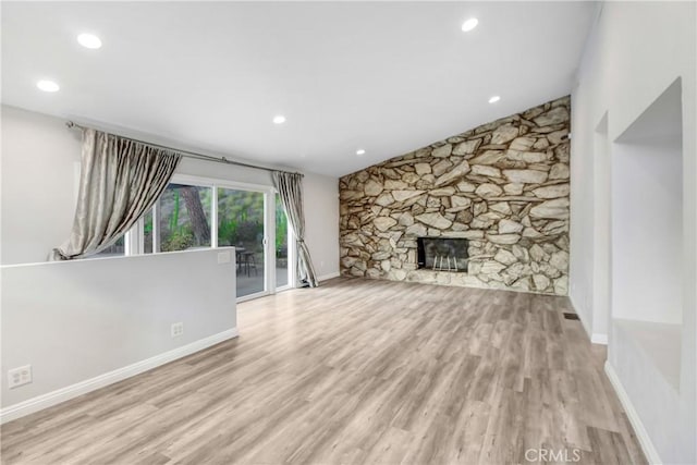 unfurnished living room featuring a stone fireplace, baseboards, and wood finished floors