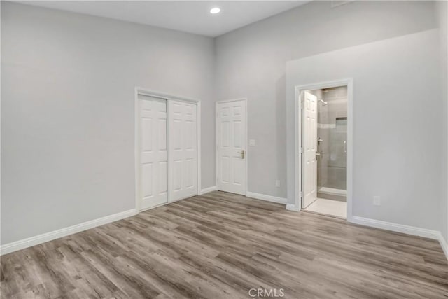 unfurnished bedroom featuring ensuite bathroom, a closet, and hardwood / wood-style flooring