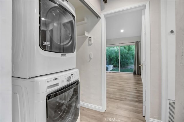 laundry area with laundry area, light wood-style floors, visible vents, stacked washer / dryer, and baseboards