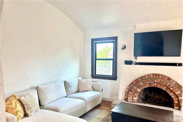 living area with vaulted ceiling, a fireplace, baseboards, and wood finished floors