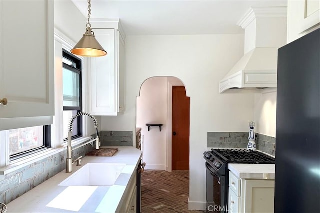 kitchen featuring arched walkways, light countertops, black appliances, premium range hood, and a sink