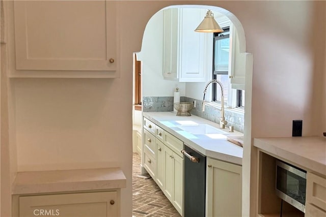 kitchen with brick floor, arched walkways, light countertops, stainless steel microwave, and a sink