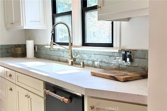 kitchen featuring dishwasher, light countertops, a sink, and white cabinetry