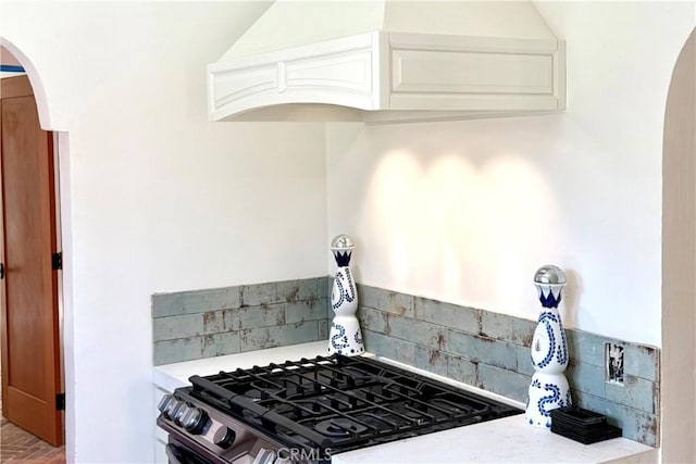 kitchen featuring arched walkways, light countertops, gas stove, and decorative backsplash