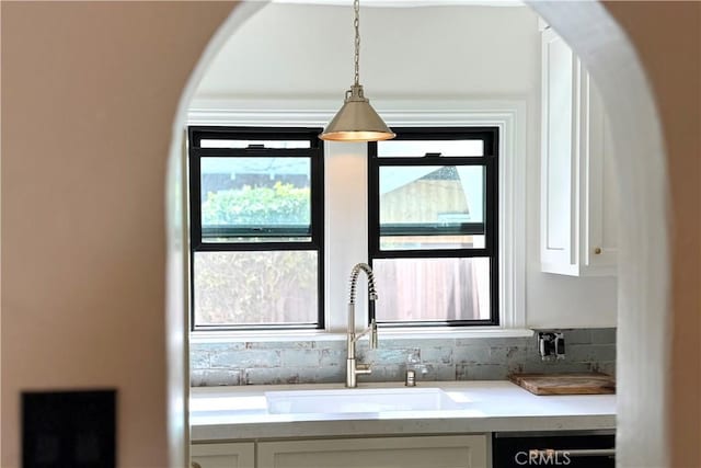 interior details with pendant lighting, light countertops, white cabinets, a sink, and dishwasher