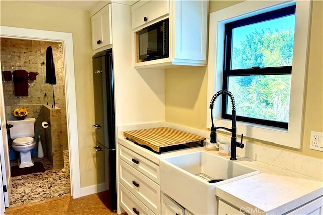 kitchen featuring black appliances, white cabinetry, light countertops, and a sink