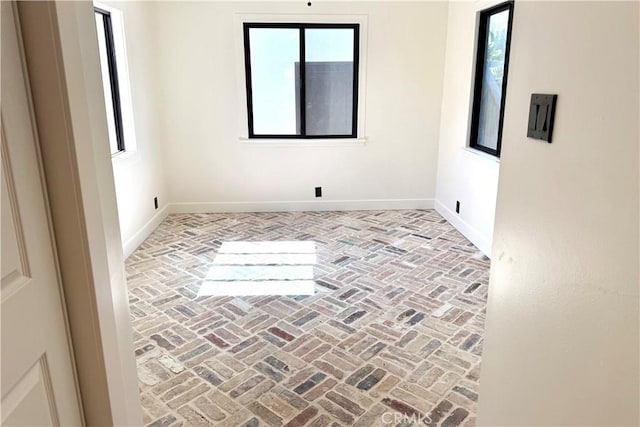 empty room featuring baseboards, brick floor, and a healthy amount of sunlight