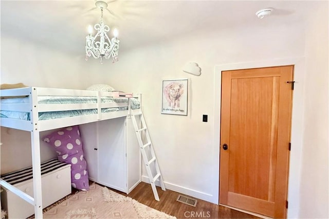 unfurnished bedroom featuring an inviting chandelier, baseboards, visible vents, and wood finished floors