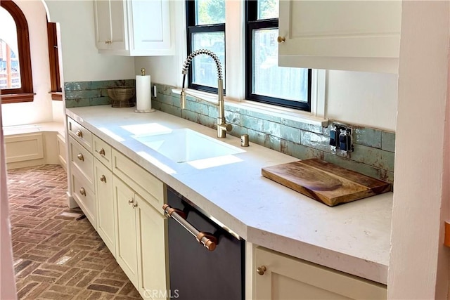 kitchen featuring brick floor, a sink, light countertops, dishwasher, and tasteful backsplash