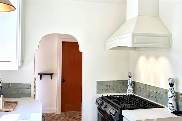 kitchen featuring arched walkways, white cabinets, light countertops, gas stove, and custom range hood