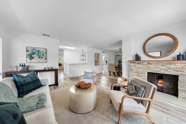 living room with a stone fireplace, an inviting chandelier, and light hardwood / wood-style floors