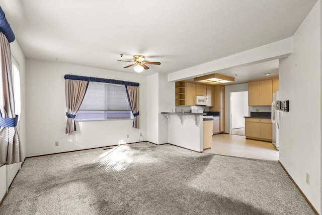 kitchen featuring a breakfast bar area, ceiling fan, light colored carpet, and white appliances