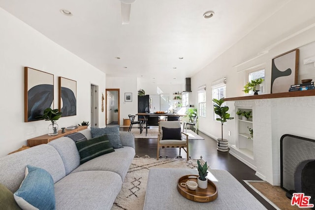 living room with hardwood / wood-style flooring, built in shelves, and a brick fireplace