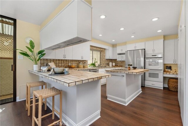 kitchen with white cabinetry, a breakfast bar area, stainless steel appliances, tile counters, and dark hardwood / wood-style floors