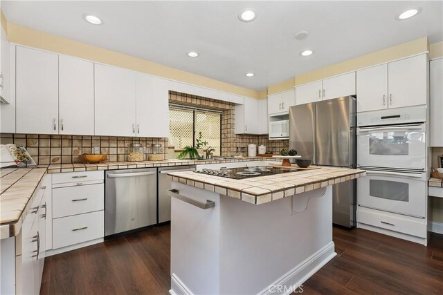 kitchen featuring appliances with stainless steel finishes, a center island, tile counters, white cabinetry, and dark hardwood / wood-style flooring