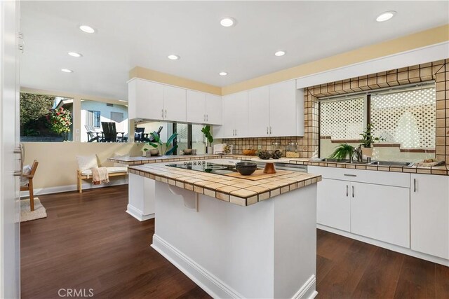 kitchen featuring tile countertops, tasteful backsplash, dark wood-type flooring, a kitchen island, and white cabinets