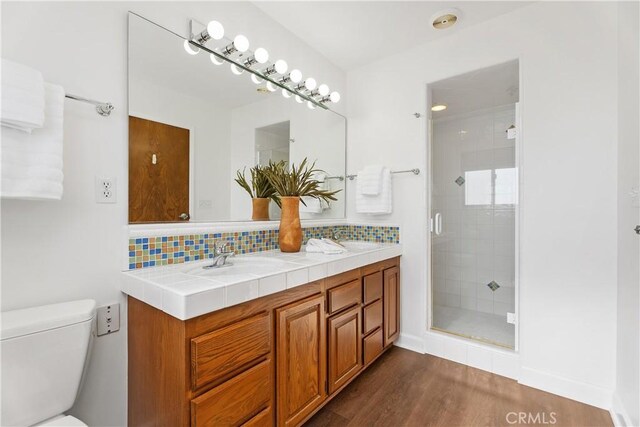 bathroom with hardwood / wood-style floors, a shower with door, vanity, backsplash, and toilet