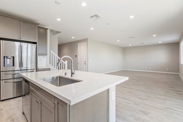 kitchen featuring stainless steel refrigerator with ice dispenser, sink, gray cabinets, and an island with sink