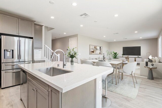 kitchen featuring sink, stainless steel fridge, gray cabinetry, and an island with sink