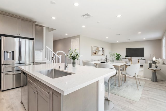 kitchen featuring visible vents, stainless steel fridge with ice dispenser, open floor plan, light stone countertops, and a sink