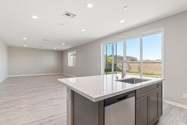 kitchen with light hardwood / wood-style floors, a kitchen island with sink, light stone countertops, stainless steel dishwasher, and sink