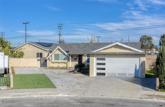 ranch-style home featuring a garage, roof mounted solar panels, fence, and concrete driveway