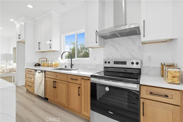 kitchen featuring stainless steel appliances, white cabinets, wall chimney exhaust hood, light hardwood / wood-style flooring, and sink