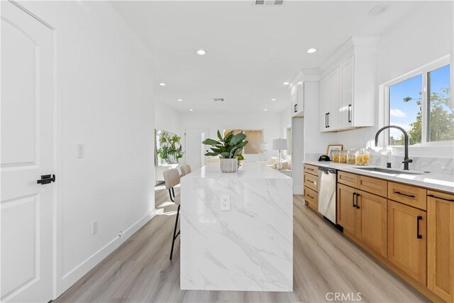 kitchen with dishwasher, sink, light wood-type flooring, a breakfast bar area, and white cabinets