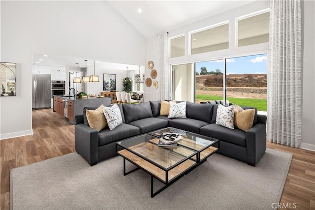 living room with high vaulted ceiling, sink, and light wood-type flooring