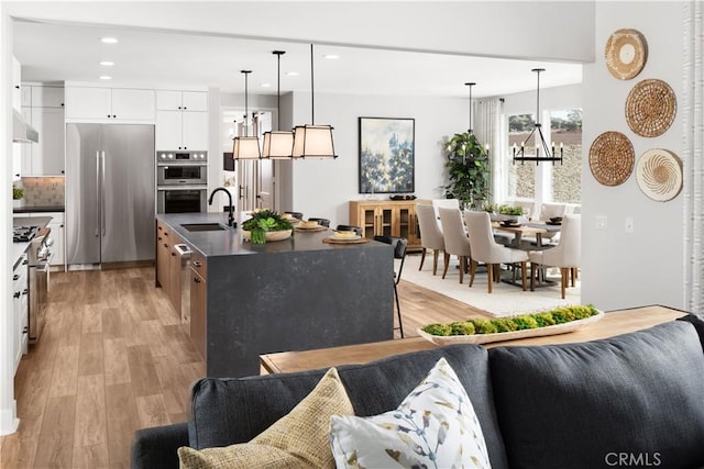 kitchen featuring hanging light fixtures, white cabinets, appliances with stainless steel finishes, and a center island with sink