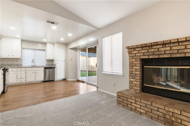 unfurnished living room featuring a brick fireplace, lofted ceiling, light colored carpet, and sink