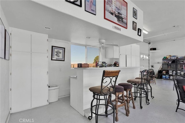 kitchen with ceiling fan, a breakfast bar, white cabinetry, and kitchen peninsula