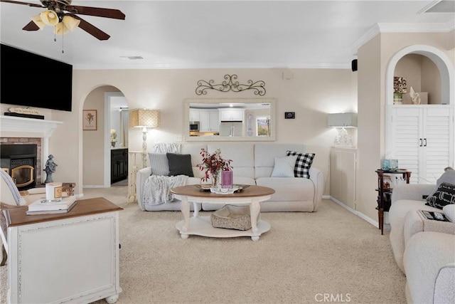 living room with light carpet, ceiling fan, crown molding, and a brick fireplace