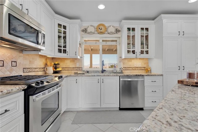 kitchen with appliances with stainless steel finishes, white cabinets, light stone counters, and sink