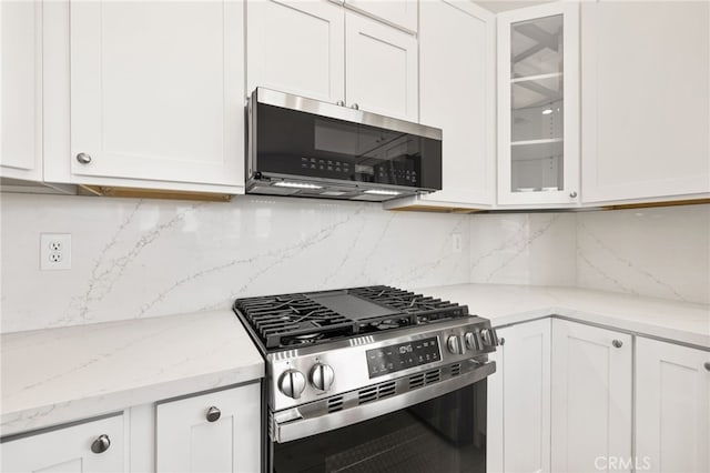 kitchen featuring light stone counters, backsplash, white cabinets, and stainless steel appliances