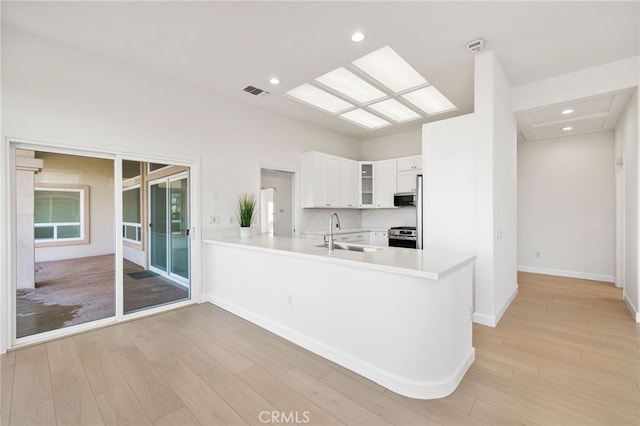 kitchen with a skylight, kitchen peninsula, stainless steel range, white cabinets, and sink