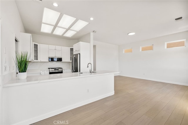 kitchen with kitchen peninsula, appliances with stainless steel finishes, tasteful backsplash, white cabinets, and sink