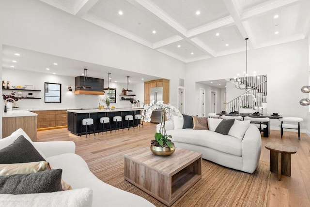 living room with coffered ceiling, a notable chandelier, a towering ceiling, light hardwood / wood-style flooring, and beamed ceiling