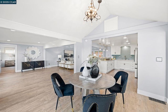 dining space featuring vaulted ceiling, sink, light hardwood / wood-style flooring, and a notable chandelier